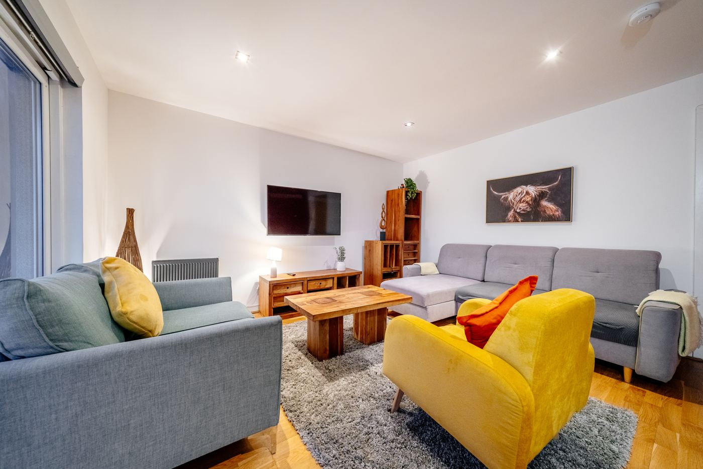 Modern living room with a yellow armchair and a Highland cow print, in a home we look after