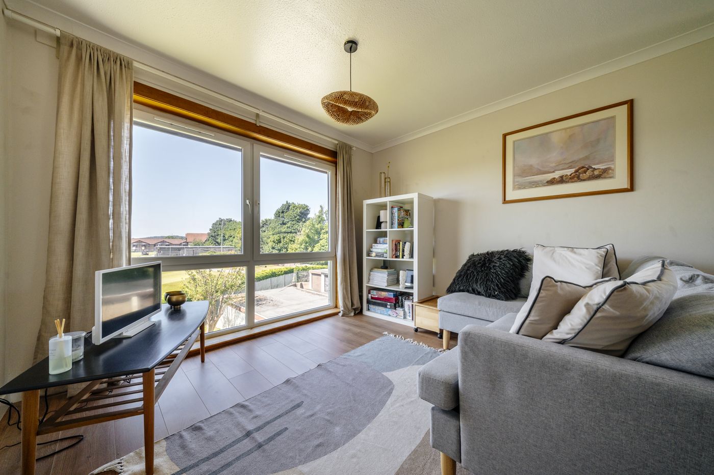 Grey sofa, bookcase and a wide window with trees outside in a home we look after in Morningside