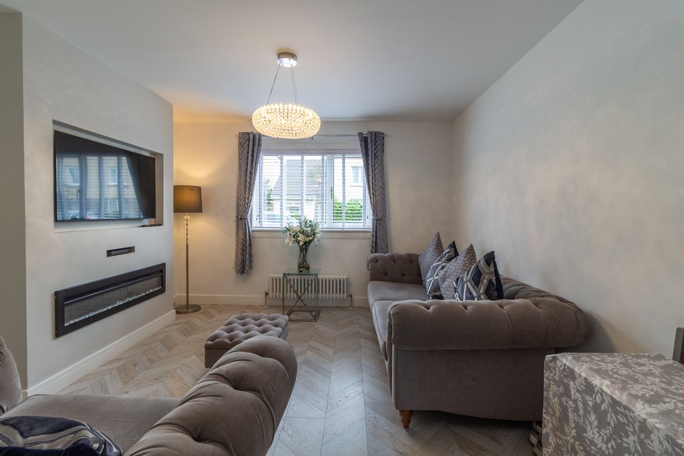 Living room with a crystal chandelier, velvet sofas and a wall fire, in a home we look after in Prestonfield
